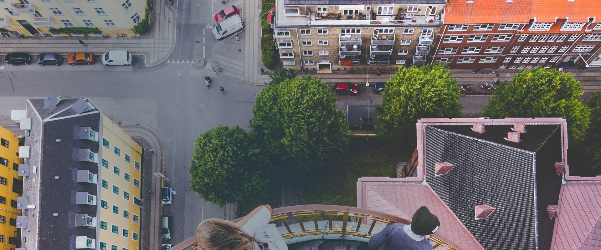 Luftfoto af fire boligblokke og et vejrkryds. På billedet er der træer, og personer der krydser vejen.