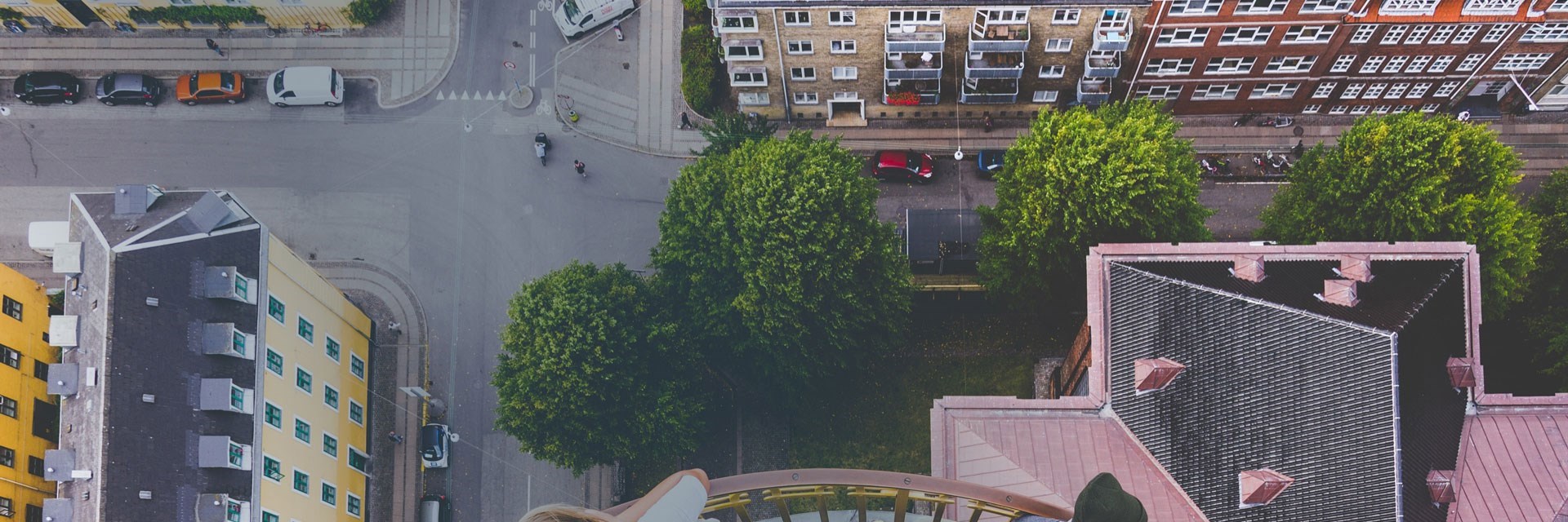 Luftfoto af fire boligblokke og et vejrkryds. På billedet er der træer, og personer der krydser vejen.